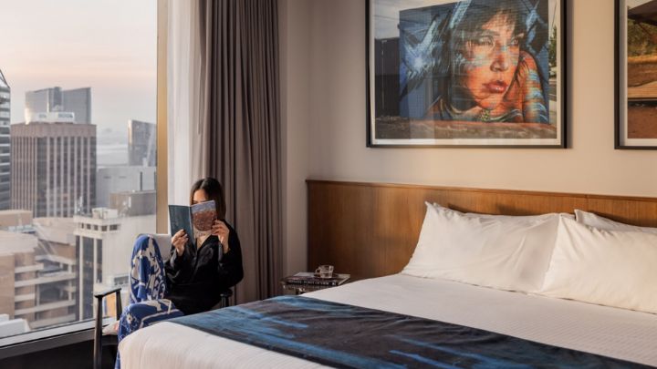 A hotel guest reading in her room next to a large city-facing window
