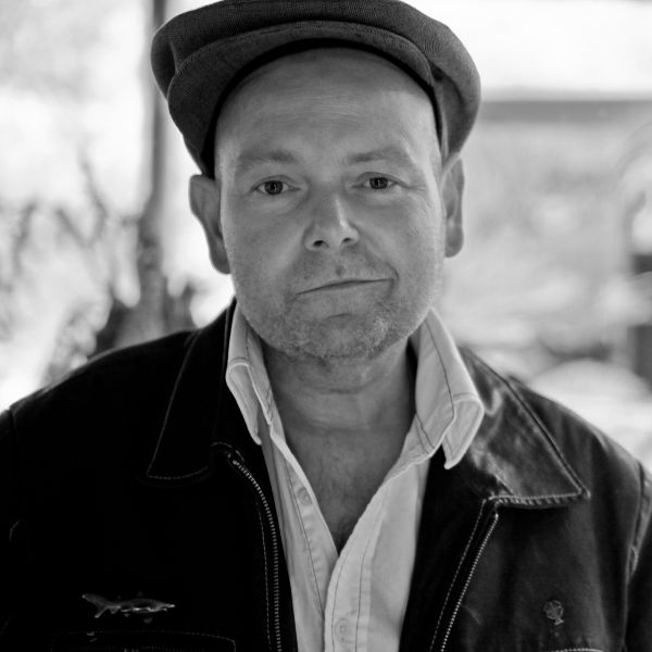 A man wearing a cap in black and white stands in front of a blurred painting
