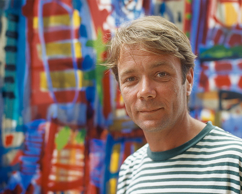 Artist David Larwill stands in front of a colourful painting