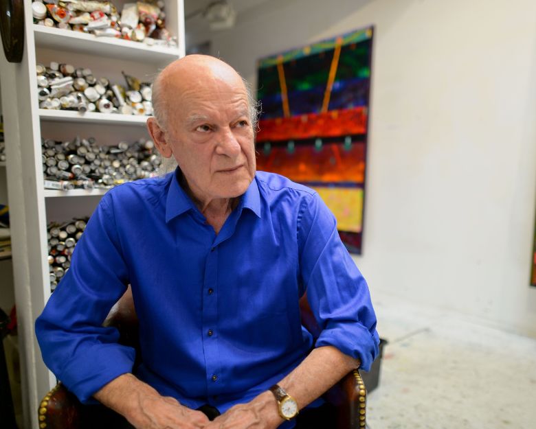 Artist Michael Johnson wears a blue shirt and sits in his art studio