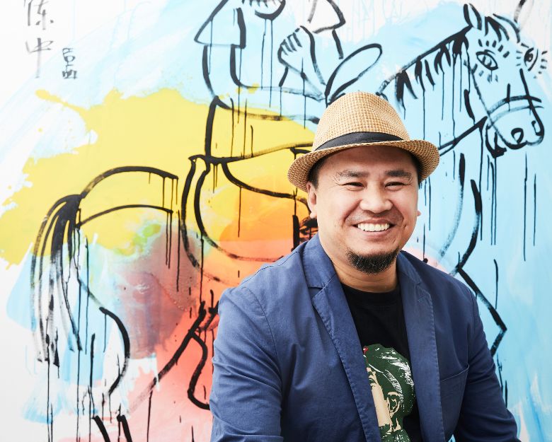 Artist Zhong Chen smiles in front of his mural of a horse